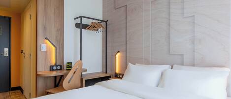 Una habitación de hotel con cama, escritorio con silla, perchero y dos lámparas de noche.