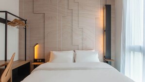 Una habitación de hotel moderna con una cama grande, un escritorio de madera, una mesita de noche con lámpara y un armario con espejo.