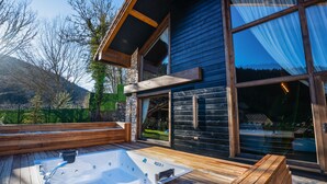 A wooden deck with a hot tub, a stone wall, and a large window overlooking a mountain. - Bi Abant Masali Village Hotel (Bolu)