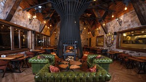 A rustic interior with a stone wall, wooden ceiling beams, and a central fireplace. - Bi Abant Masali Village Hotel (Bolu)