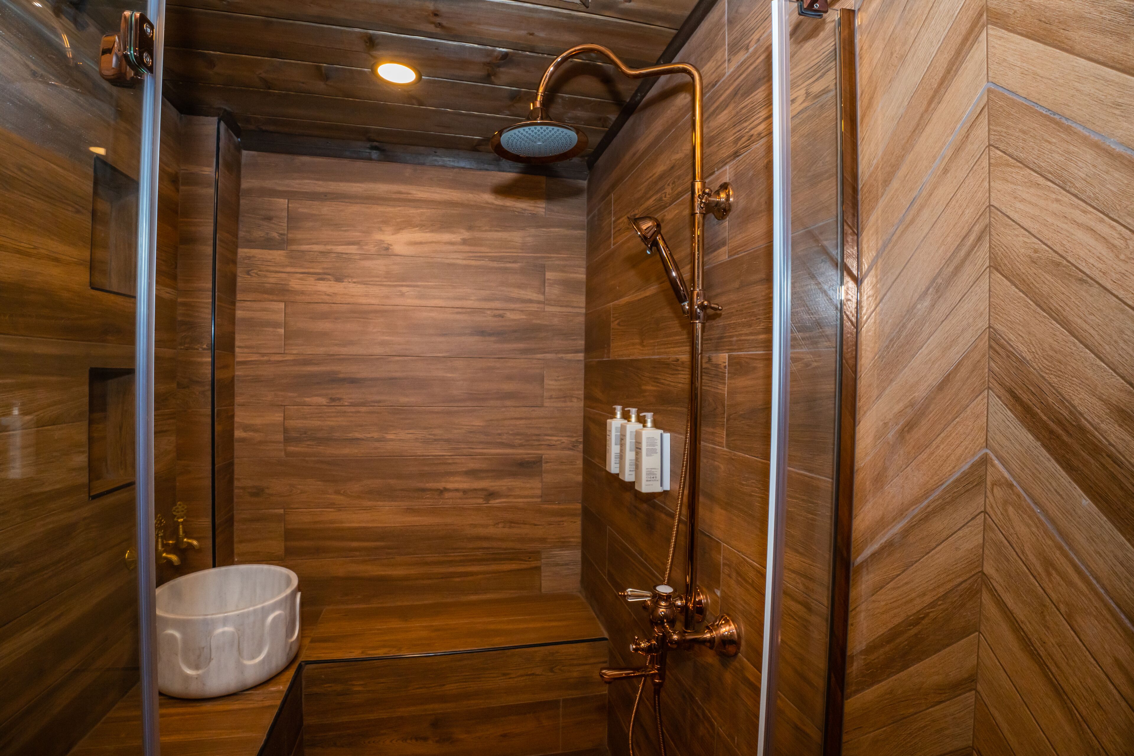 A wooden interior with a shower, a sink, and toiletries on the wall.