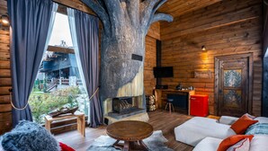A cozy log cabin interior with a large tree sculpture, a fireplace, a sofa, and a dining table. - Bi Abant Masali Village Hotel (Bolu)