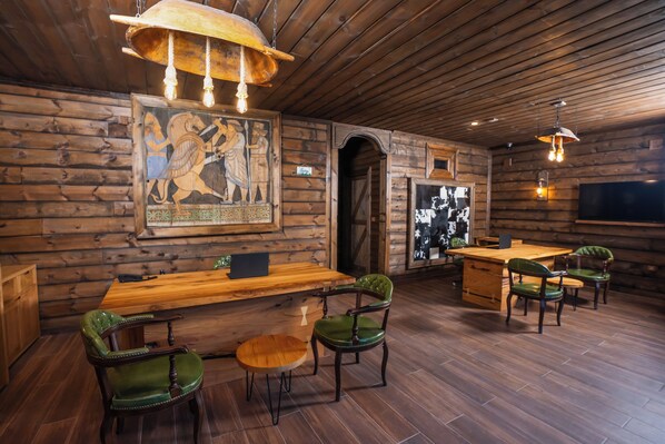 Un interior rústico de madera con un largo banco de madera, sillas tapizadas de verde, una mesa de madera y un cuadro colgado.
