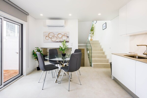 A modern kitchen with a glass dining table, black chairs, a potted plant, and a staircase leading to an upper level. - Casa Bela / (Almancil)