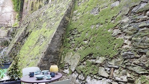 A stone wall with moss, a round table with chairs, and a yellow lamp. - Loft Garibaldi by Wonderful Italy (Genoa)