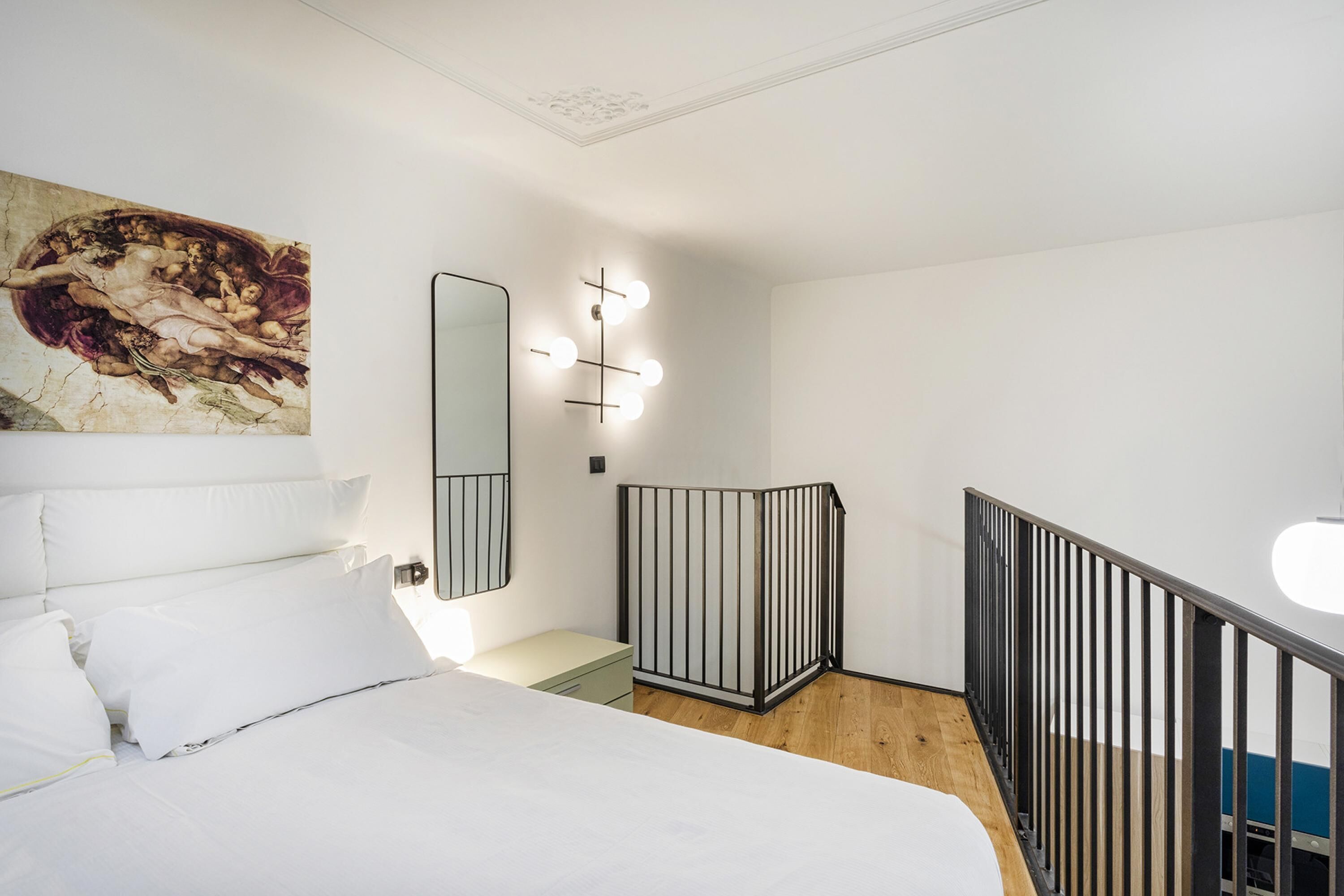 Un dormitorio con cama, mesita de noche, espejo y lámpara de pared.