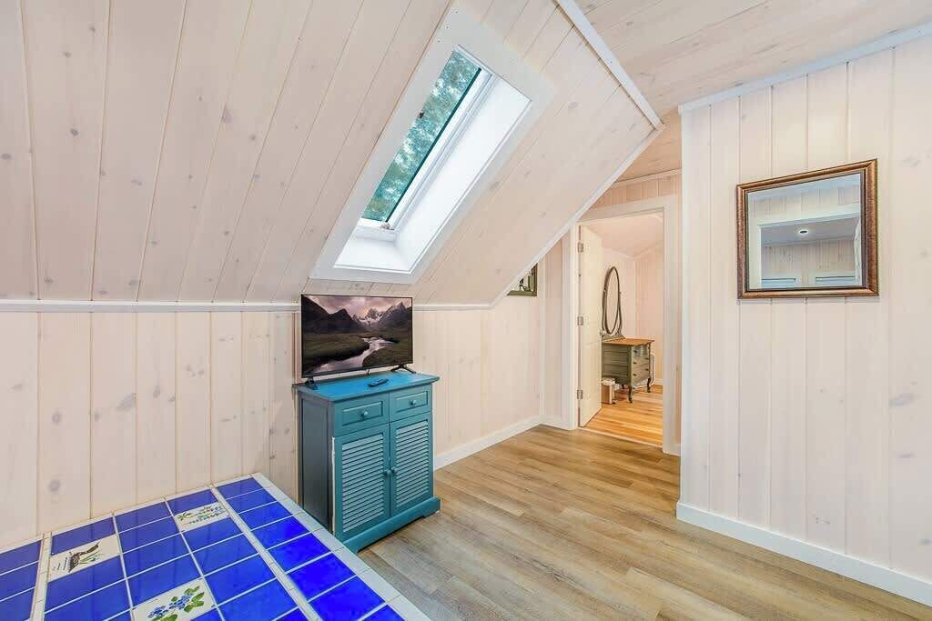Ein Zimmer mit schrägverdeckter Decke, einem Oberlicht, einem Fernseher auf einem Schrank und einem blau gefliesten Boden.