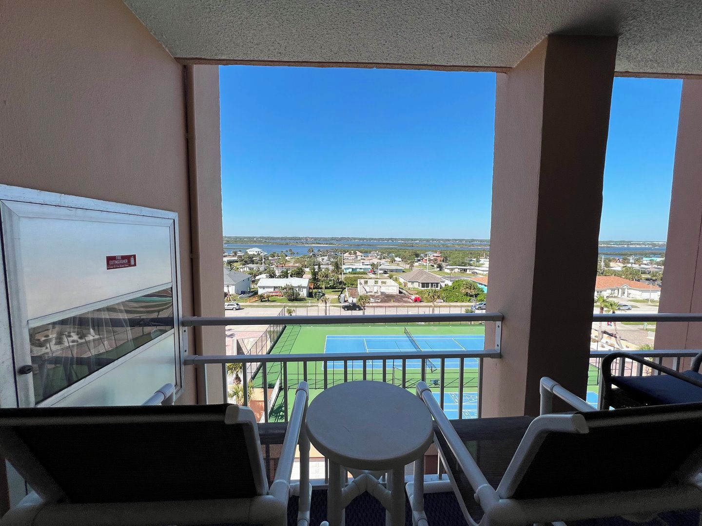 Een balkon met uitzicht op een tennisbaan en omliggende gebouwen.