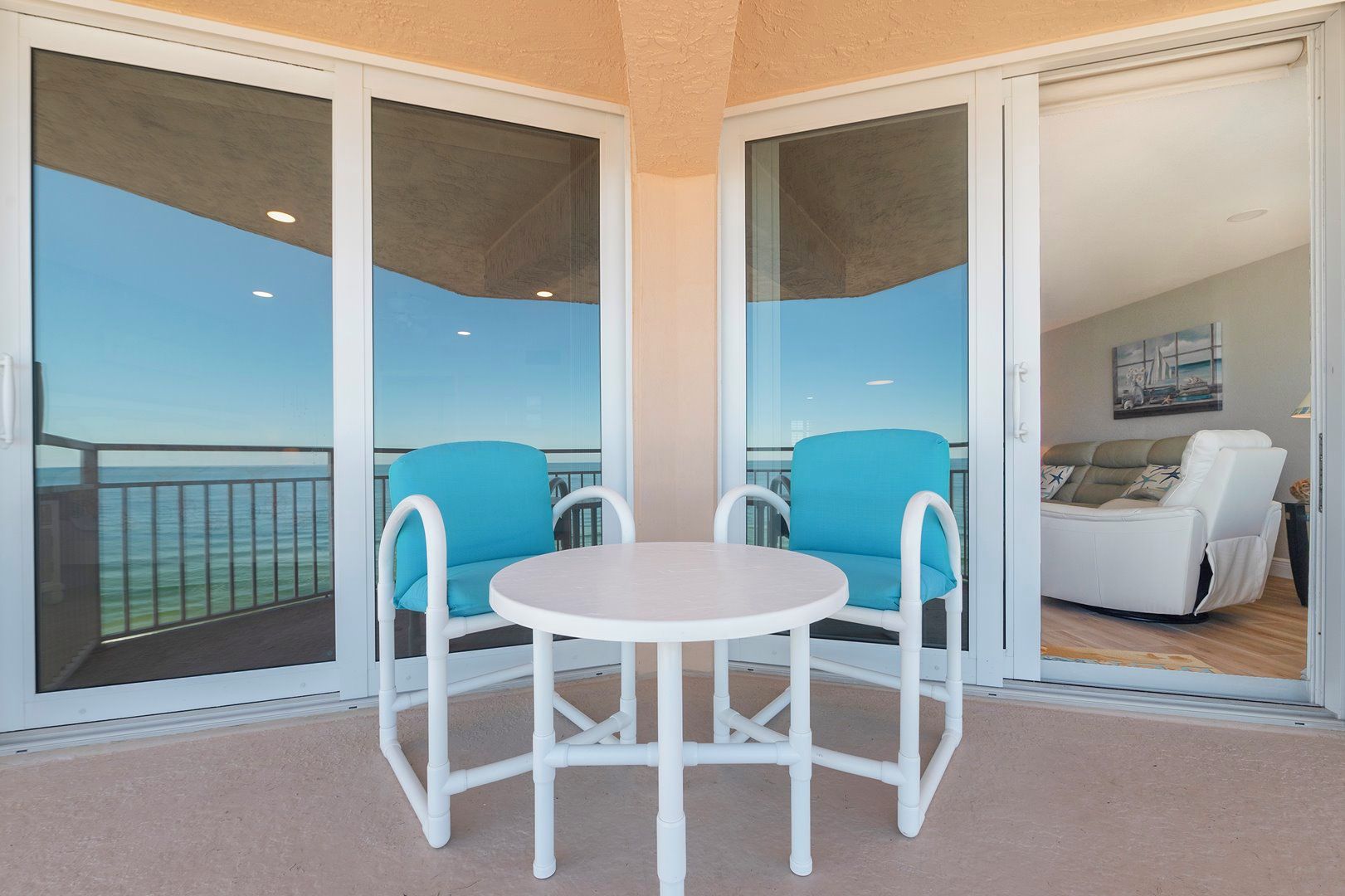 A balcony with two chairs and a table, a sliding glass door, and a view of the sea.