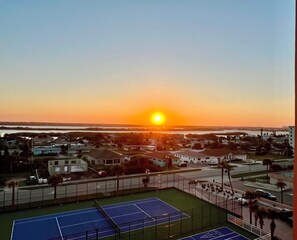 Un court de tennis offrant une vue sur un quartier résidentiel et un coucher de soleil en arrière-plan.