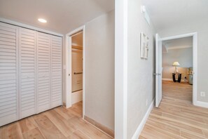 Un pasillo con piso de madera, paredes blancas y una puerta blanca que da a un baño.