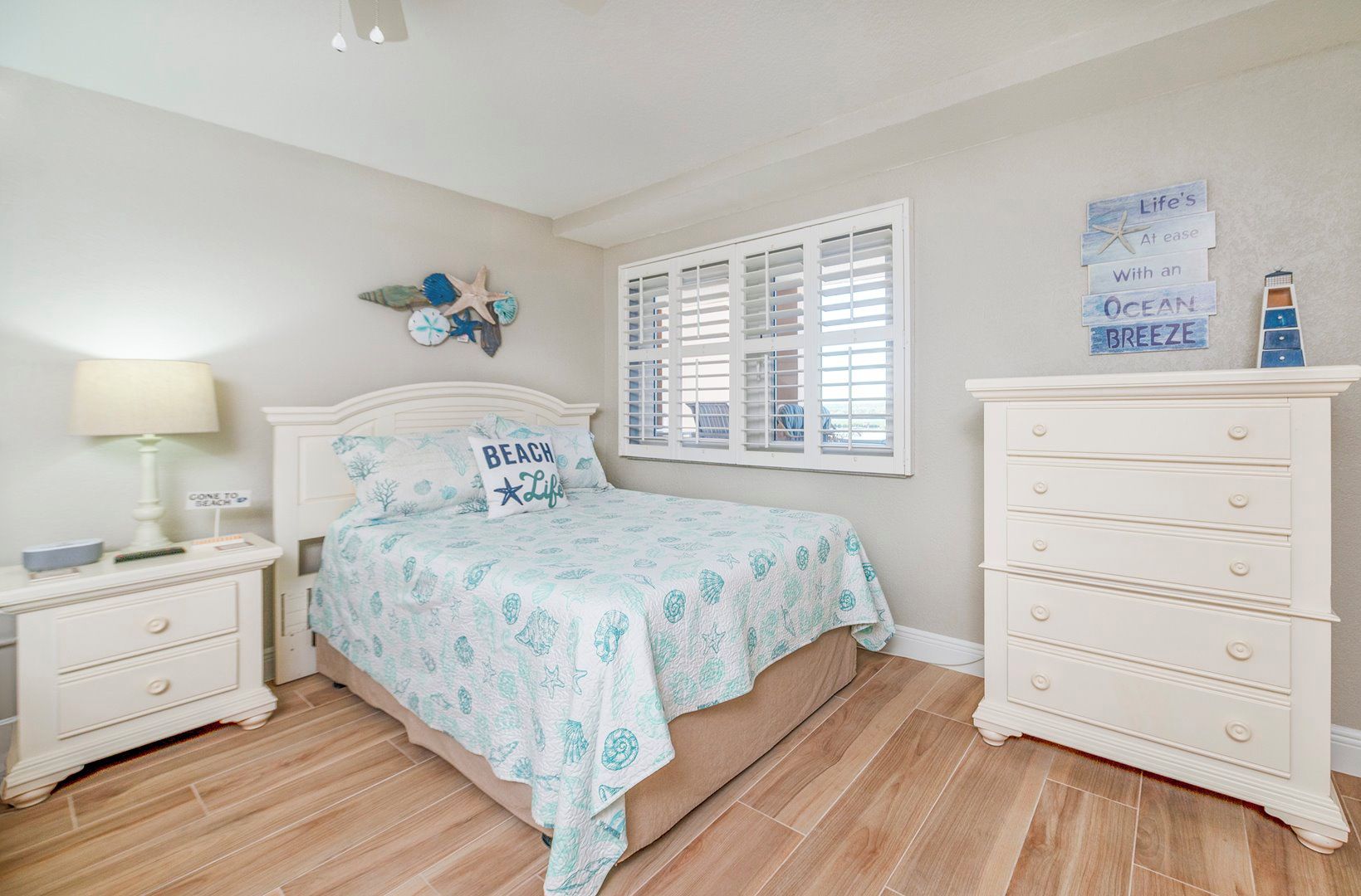 A bedroom with a bed, nightstands, a dresser, a window with shutters, and wall decorations.