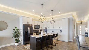 Une cuisine moderne dotée d’un îlot central, de tabourets de bar et de luminaires suspendus.