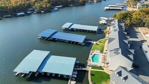 Vue aérienne d’une propriété au bord du lac, avec des bateaux amarrés, une piscine et un grand bâtiment doté d’un toit en pente.