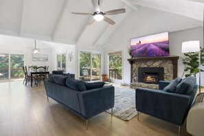 Relax in this stylish living room with a high ceiling, ceiling fan, and large flat-screen TV above a stone fireplace. Enjoy the view from the large window.