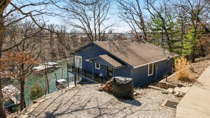 A blue house with a sloped roof, a covered grill, and a gravel driveway. - Spacious Home & Lake Access, Lake Views Throughout (Lake Ozark)