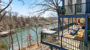 A two-story building with a balcony overlooking a river. The balcony has outdoor furniture and a table. - Spacious Home & Lake Access, Lake Views Throughout (Lake Ozark)