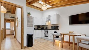 Een moderne keuken met witte kasten, een eethoek met een houten tafel en stoelen, en een aan de muur bevestigde televisie.
