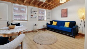 Een gezellige woonkamer met een blauwe bank, een ronde tafel en een dakraam erboven.