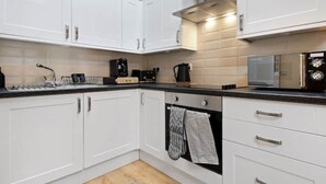 Een moderne keuken met witte kastjes, een inbouwoven, een magnetron en een koffiezetapparaat.