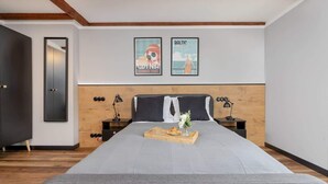 Ein modernes Schlafzimmer mit einem großen Bett, einem Holzkopfende, zwei Bildern an der Wand und einem Tablett mit Snacks auf dem Bett.