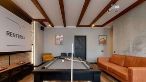Ein Billardtisch in einem Raum mit Holzbalkendecke, einer Couch und einer Ziegelwand.