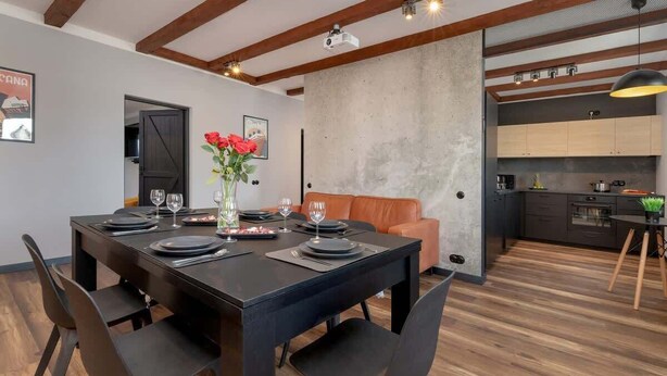 Ein moderner Essbereich mit einem schwarzen Tisch, gedeckt für vier Personen, einer Couch und einer Küche im Hintergrund.