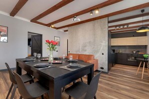 A modern dining area with a black table set for four, a sofa, and a kitchen in the background. - Spacious Apartment | 3 Bedrooms | Billiard Table (Gdynia)
