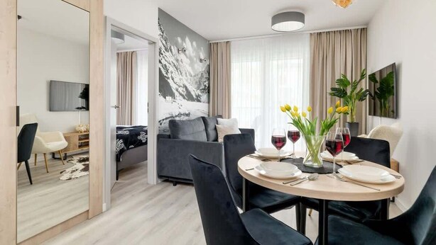 Et moderne hotelværelse med spiseplads, sofa, fladskærms-tv og et stort vindue med gardiner.