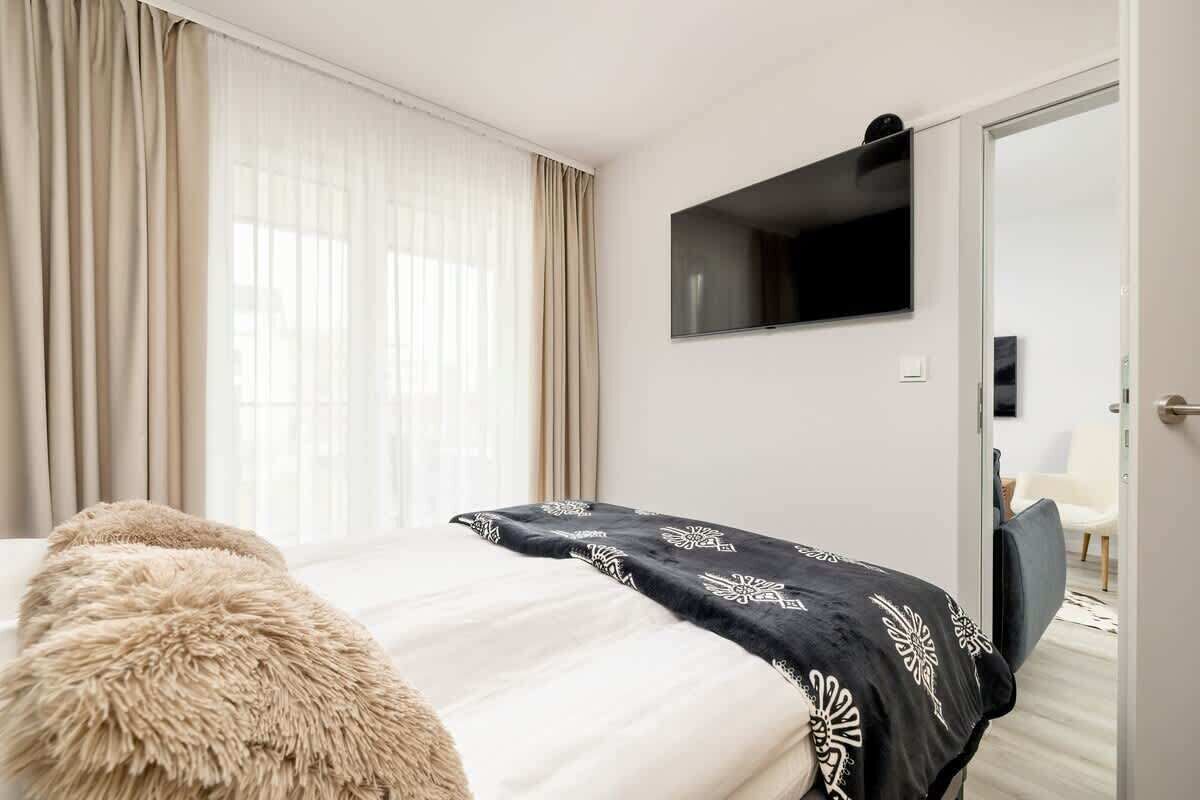 A hotel room with a bed, a television mounted on the wall, and a door leading to another room.
