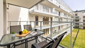 En balkon med et glasbord, stole og et fadebord med frugt.