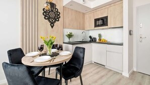 Et moderne køkken med træskabe, en sort mikrobølgeovn og et spiseområde med sorte stole og et rundt bord dækket til to personer.