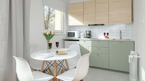 A modern kitchen with white cabinets, a microwave, and a coffee maker. There is a dining table with white chairs and a vase of flowers.