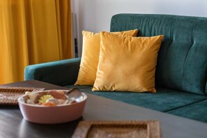 Un canapé vert avec deux coussins jaunes, un plateau en bois et un bol de nourriture sur une table.