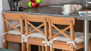 A kitchen with wooden chairs, a coffee machine, and a bowl of fruit.
