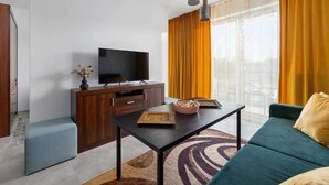 A modern living room with a flat-screen TV, wooden cabinet, sofa, coffee table, and a large window with curtains.