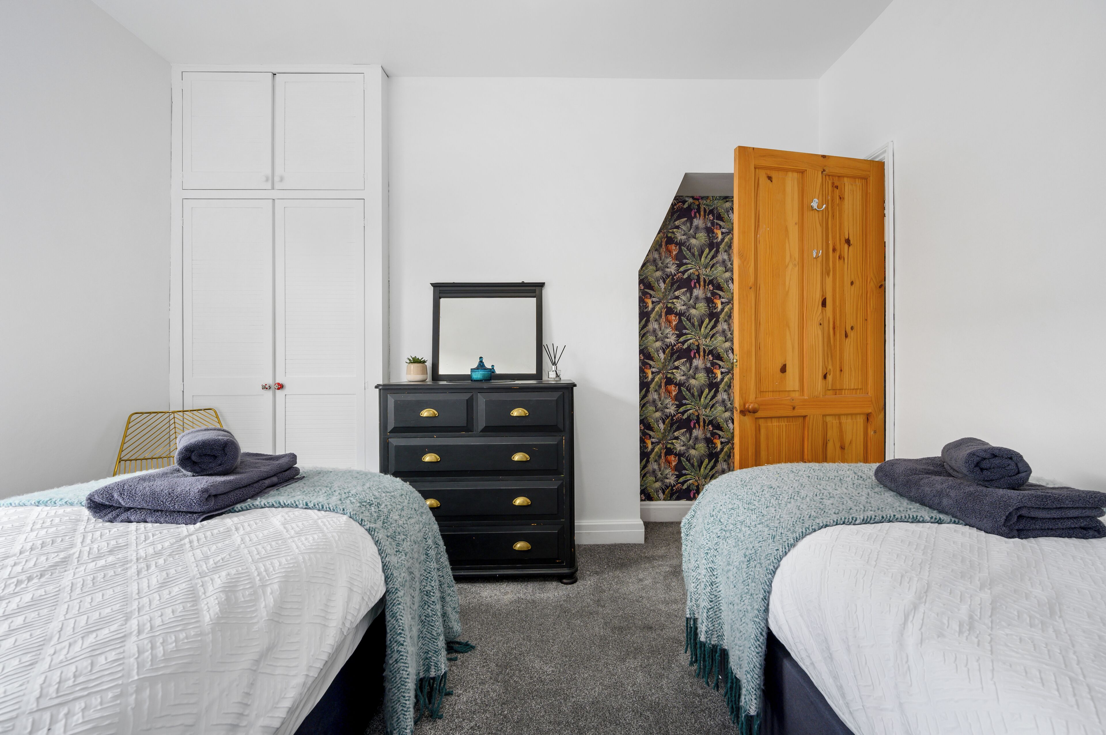 A bedroom with two beds, a dresser, a mirror, and a wardrobe.