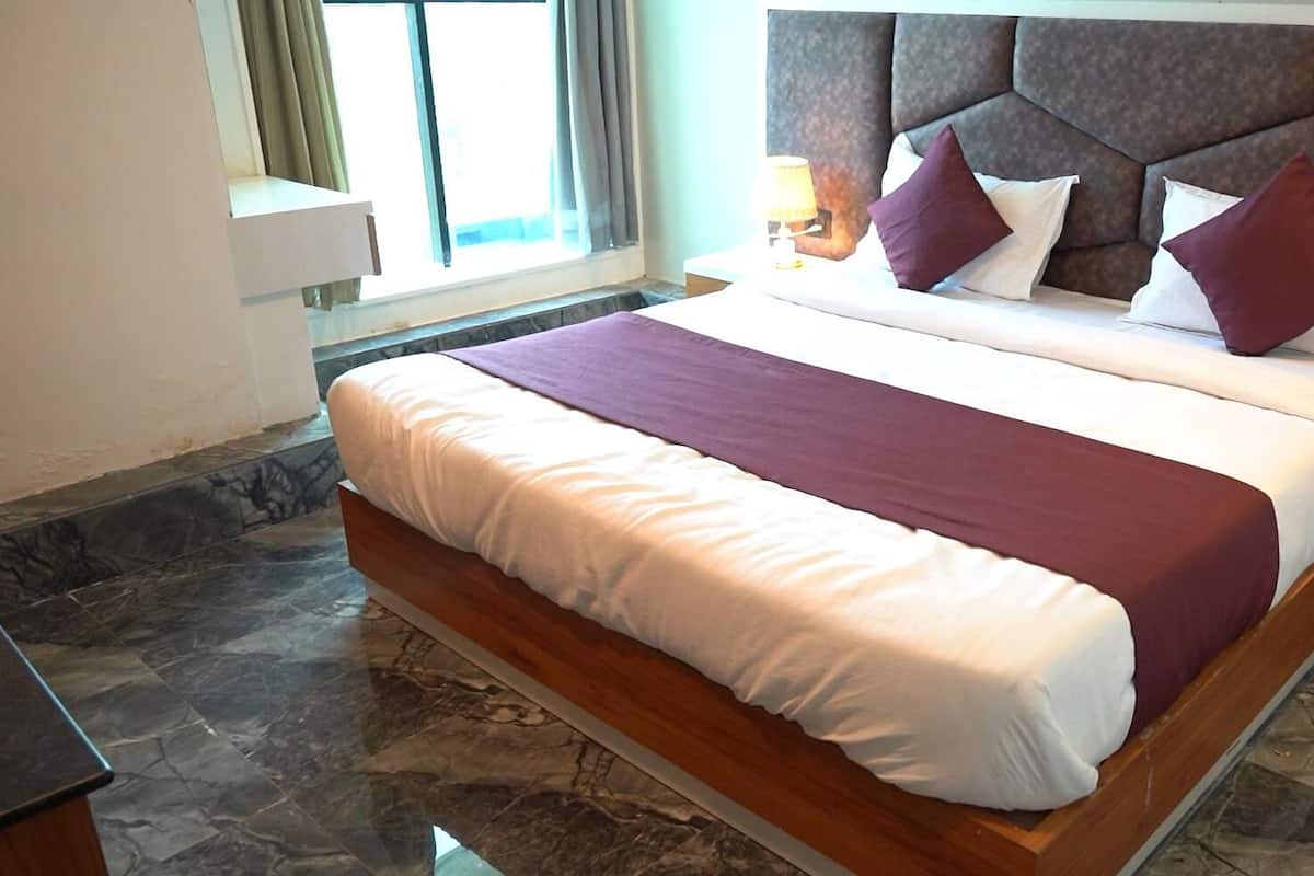 Una habitación de hotel moderna con una cama grande, una mesita de noche, una lámpara y un ventanal con cortinas.