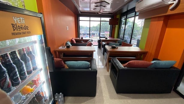 A restaurant interior with a refrigerated beer display, seating arrangements, and large windows.