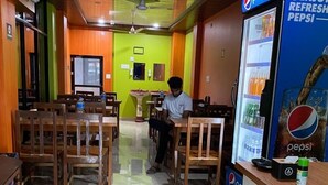 A restaurant with wooden tables and chairs, a Pepsi refrigerator, and a ceiling fan.