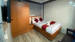 A bedroom with a wooden wardrobe, a bed with white bedding and red accents, a ceiling fan, and a wooden floor.