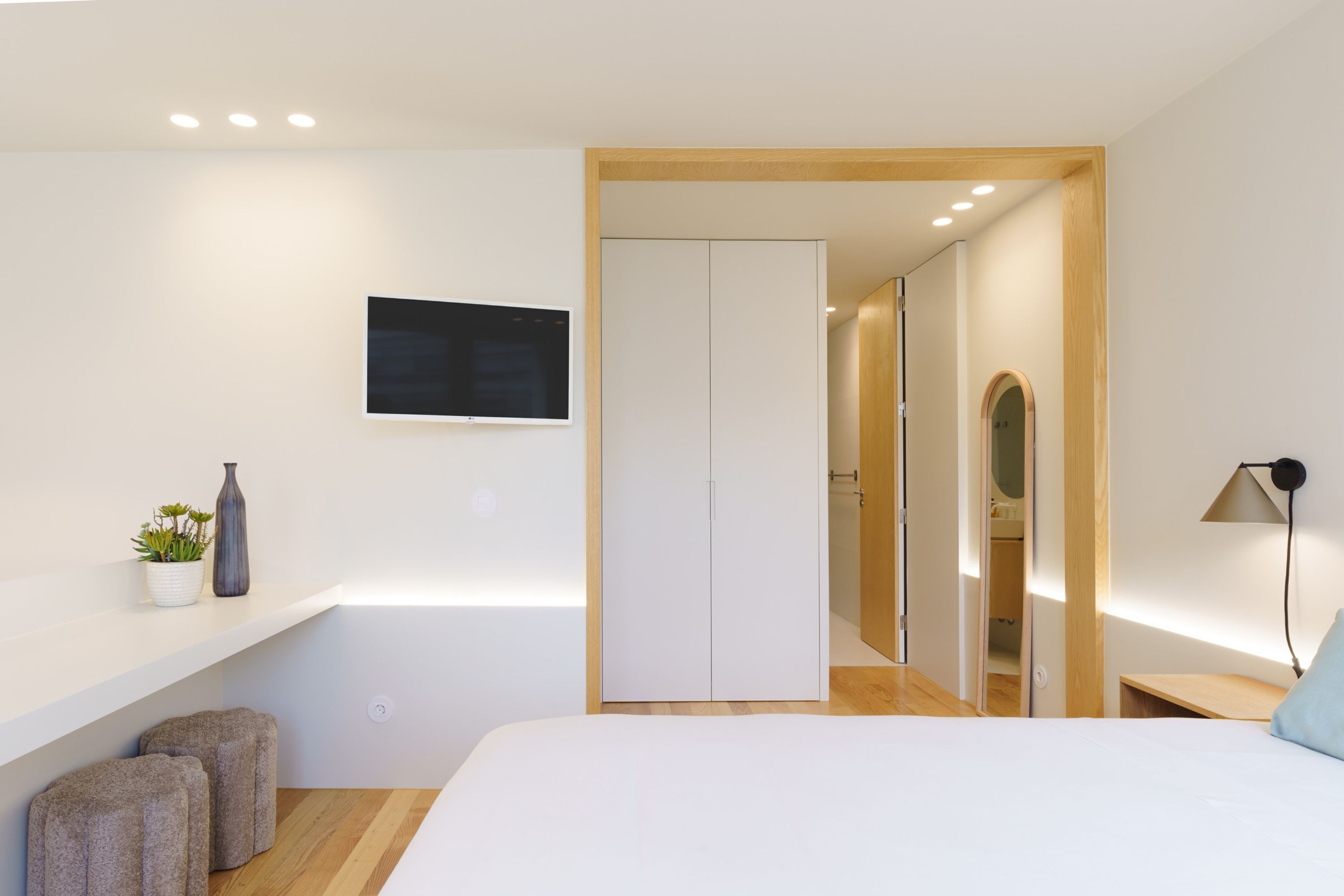 Une chambre moderne comprenant un lit, une télévision, une armoire et un petit coin salon avec des tabourets.