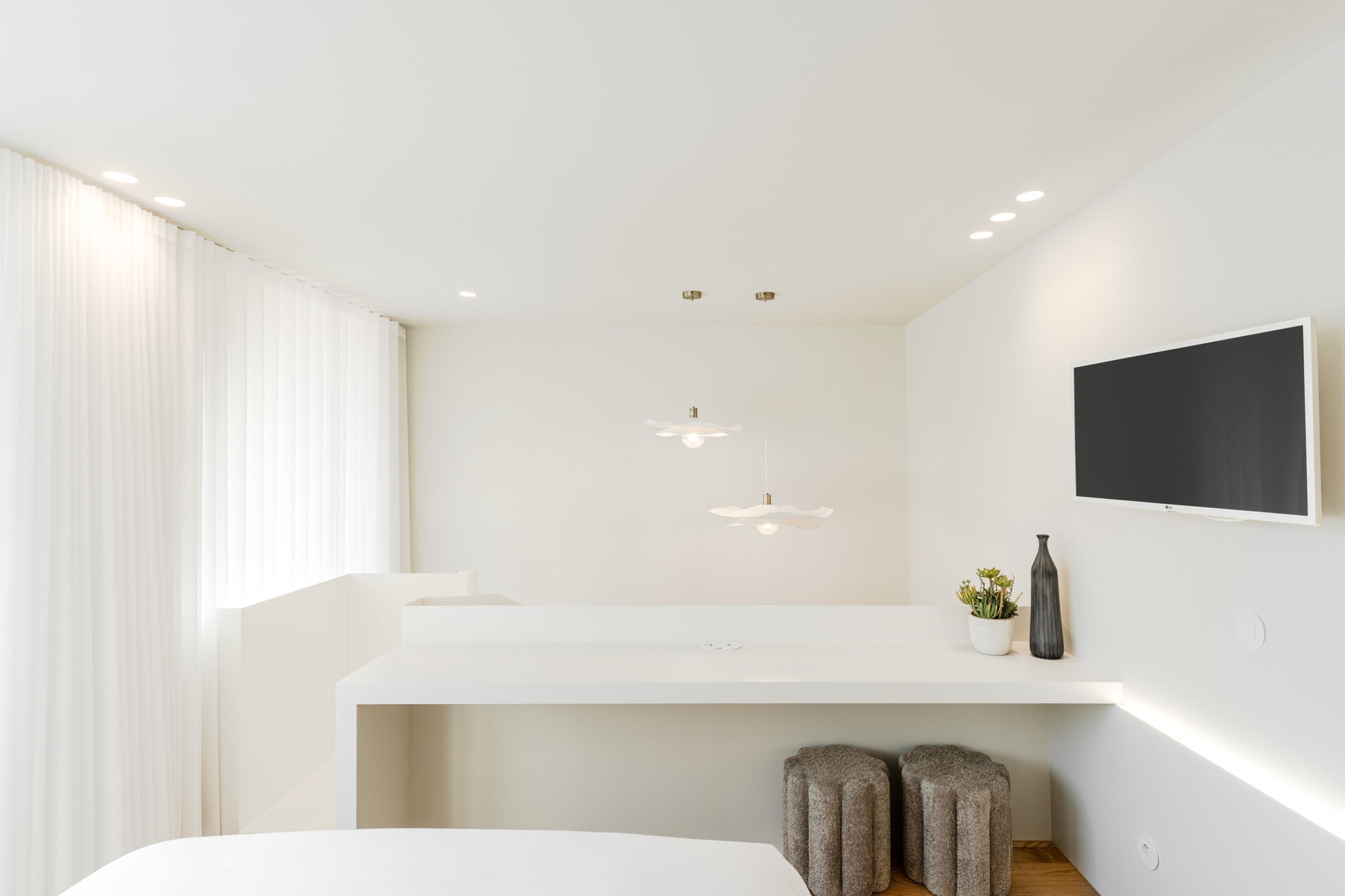 A modern hotel room with a large bed, a white vanity, a flat-screen TV mounted on the wall, and a small potted plant.