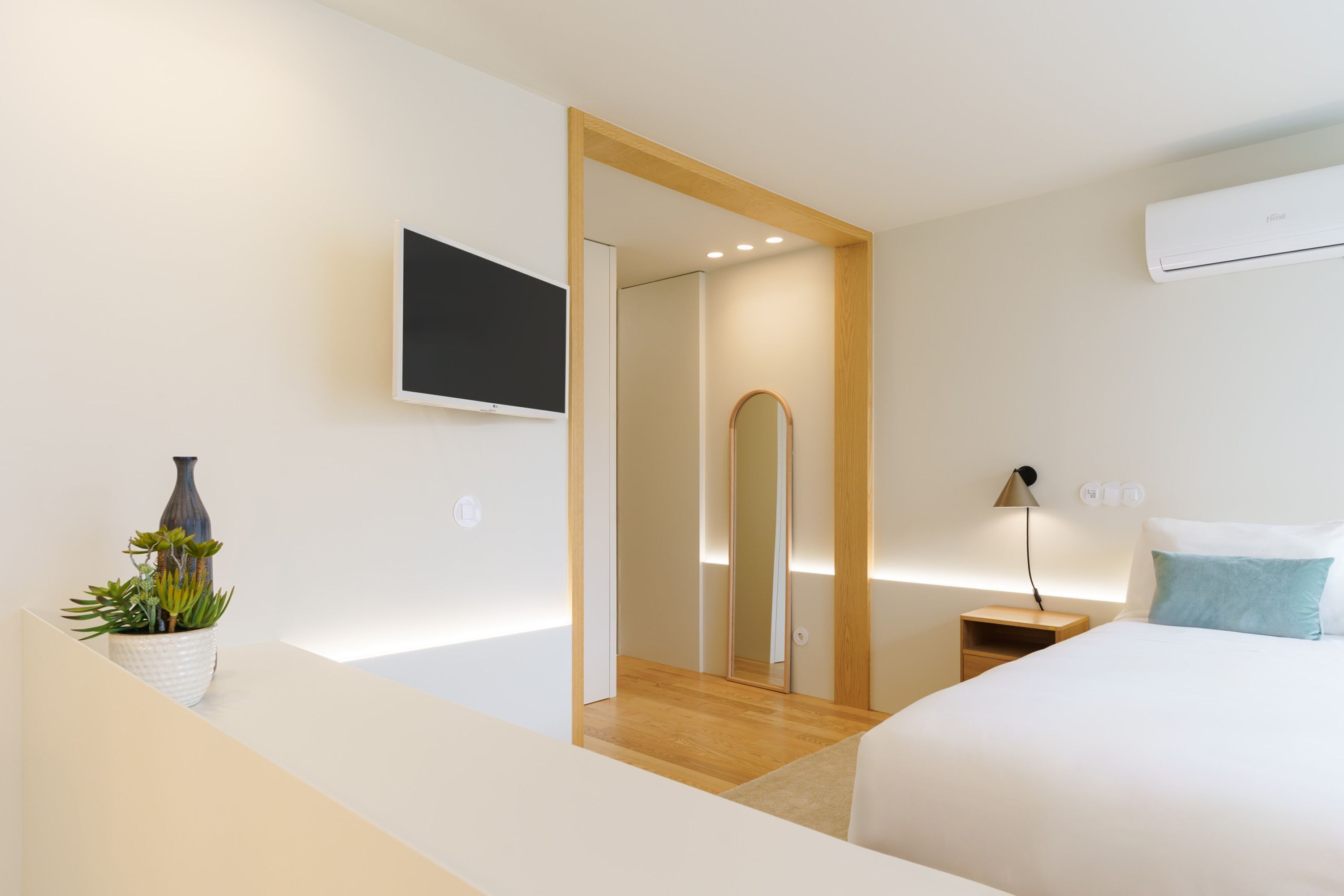 Ein modernes Hotelzimmer mit einem Bett, Nachttisch, Lampe und einem Blumentopf.