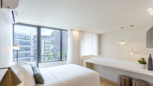 A modern hotel room with a large bed, a bedside table, a vanity with a mirror, and a view of the city through large windows. - Feel Porto Corporate Housing Boavista I (Porto)