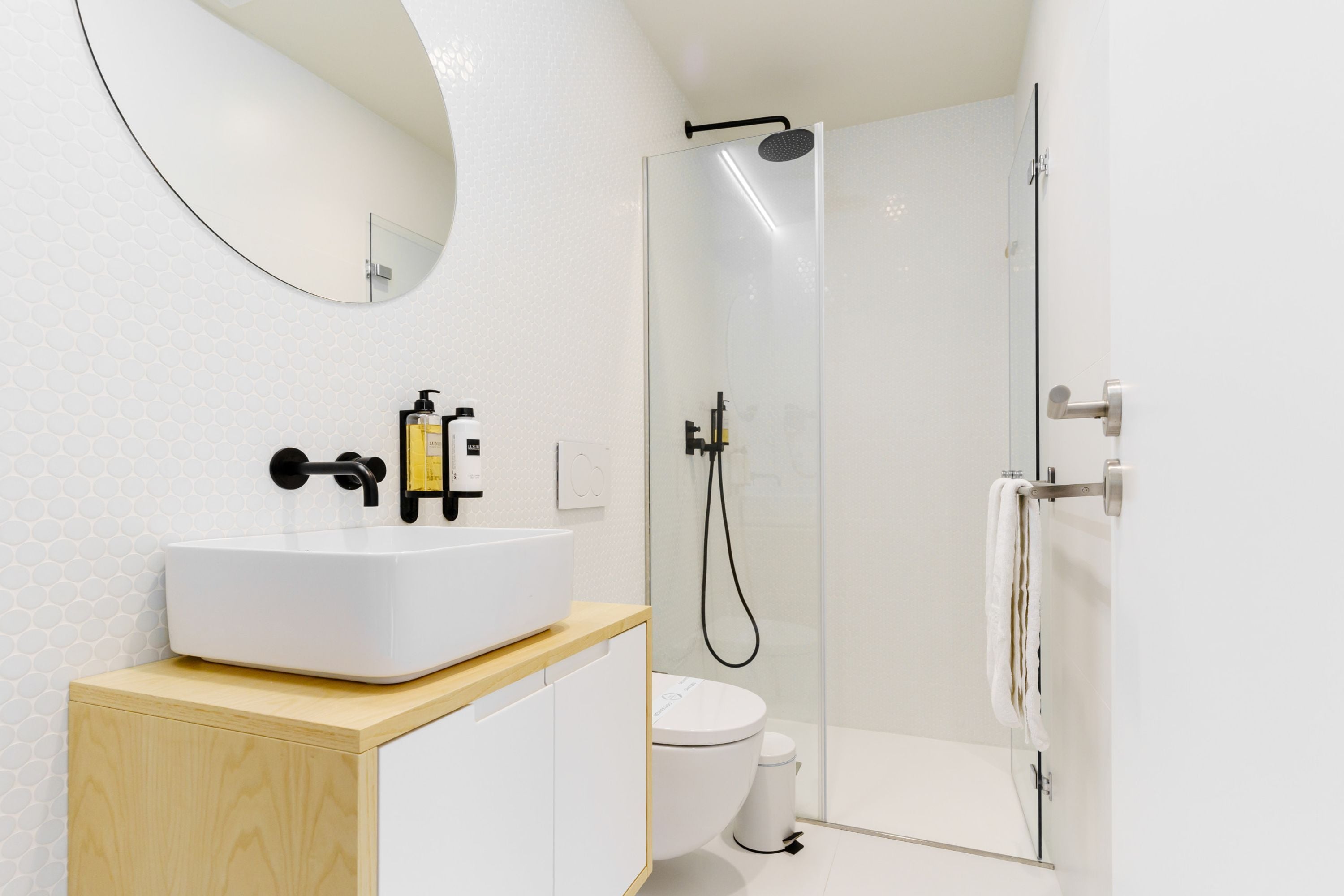 Un baño moderno con lavamanos blanco, espejo, inodoro y ducha con mampara de vidrio.