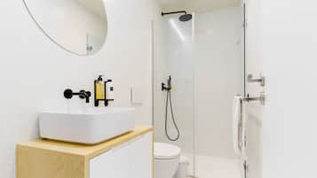 Un baño moderno con lavamanos blanco, espejo, inodoro y ducha con mampara de vidrio.