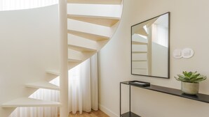 A modern staircase with white railings and a wooden floor. A black console table with a plant and a mirror is against the wall. - Feel Porto Corporate Housing Boavista I (Porto)