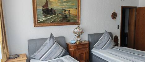 A bedroom with two beds, a nightstand, a lamp, a painting, and a wooden wardrobe.