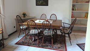Ein Essbereich mit einem Holztisch und Stühlen, einem gemusterten Teppich, einem Gemälde an der Wand und einem Bücherregal mit Büchern und Dekoration.